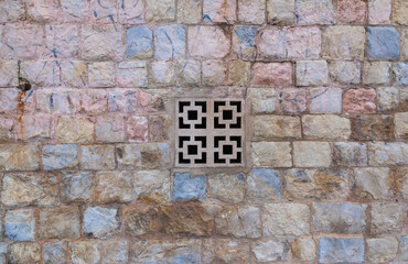 Fototapeta na wymiar Antique wall made of natural stone with a lattice stone insert in the hole in the middle in the form of crosses and squares.