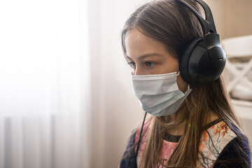 A child in a medical mask with headphones looks forward in a bright room. close-up portrait