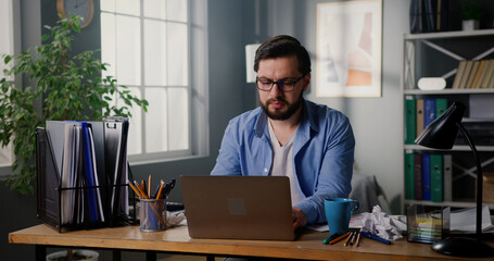 Obraz premium Focused serious businessman looking at computer screen working on laptop at home office. Freelancer doing online job. Close up shot.