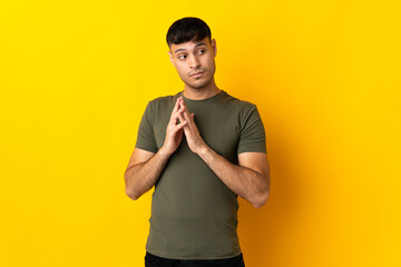 Young Colombian man isolated on yellow background scheming something