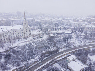 Snow-covered streets of the city from the air. The roads are covered with snow. White chapel in the snow. Snowstorm over the square. Winter fairy tale in the city from the air.