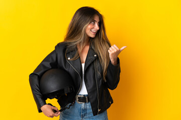 Woman holding a motorcycle helmet isolated on yellow background pointing to the side to present a...