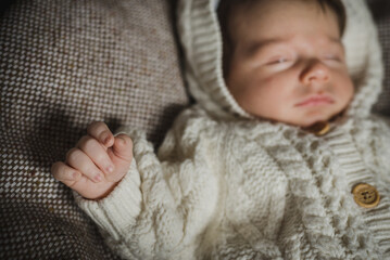 A portrait of little newborn in white cozy knitted overall laying on beige woollen plaid. Sleeping...