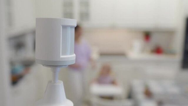 Smart home wireless motion sensor for alarm system and smart home automation, small plastic white motion detector installed in the living room. High quality 4k footage