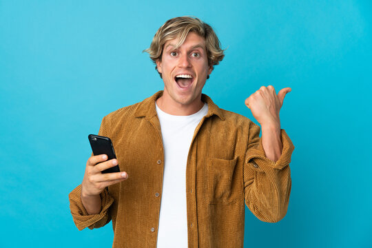 English man over isolated blue background using mobile phone and pointing to the lateral
