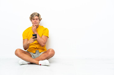 Young English man sitting on the floor thinking and sending a message