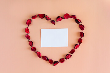 Obraz premium Petals and a card in the shape of a heart on a coral background. Valentines day, wedding, anniversary concept. 