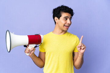 Young Venezuelan man isolated on purple background holding a megaphone and intending to realizes the solution