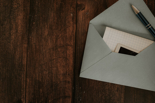 An envelope with a letter and a pen lie on a wooden table.