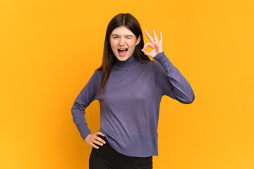 Young Ukrainian girl isolated on yellow background showing ok sign with fingers