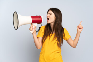 Naklejka premium Young Ukrainian girl isolated on white background shouting through a megaphone to announce something in lateral position
