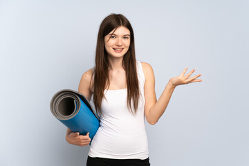 Young Ukrainian sport girl going to yoga classes while holding a mat extending hands to the side for inviting to come