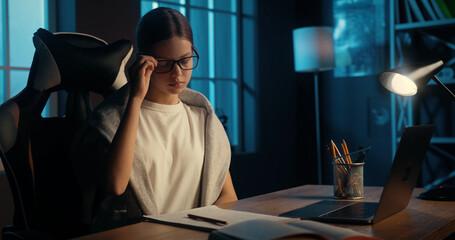 Tired bored smart young teenage girl takes off glasses to rest from study remotely and watching video lesson. Education during pandemic.