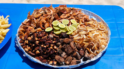 Large plate with a mix of grilled seafood shrimp, octopus, tuna fish, squid. BBQ exotic food on the beach.