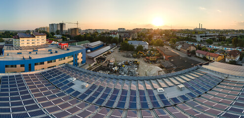 Aerial view of blue photovoltaic solar panels mounted on industrial building roof for producing green ecological electricity at sunset. Production of sustainable energy concept