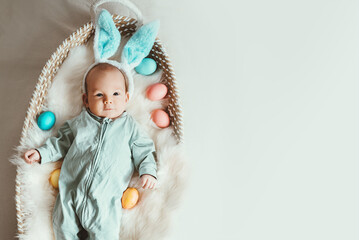 Cute baby Easter bunny. Little baby boy with bunny ears and Easter eggs in wicker basket in white fur. Symbol of Easter holiday, birth, spring, religion.