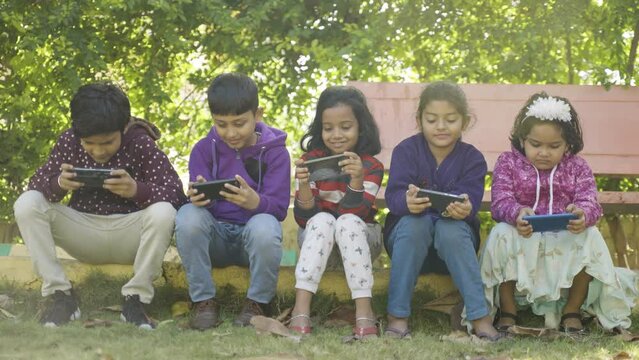 Group of kids busy using mobile phone while sitting at park - concept of smartphone addiction, playing video game, reduced physical activity and impact of technology,