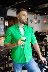 Handsome man in green holding his beer in a pub for St. Patrick's Day