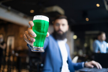 A man holding green glass of beer in a pub during St. Patrick's Day