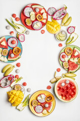 Exotic fruits on colorful plates and white table. Cirle frame. Watermelon, ananas, pitaya, banana, passion fruits, lime and mango. Healthy and delicious tropical fruits. Top view with copy space.