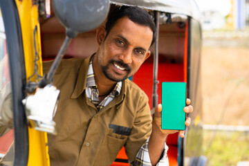Focus on mobile, smiling young rickshaw driver showing green screene mobile phone by lookling camera - concept of online booking service, promotion and advertising. - obrazy, fototapety, plakaty