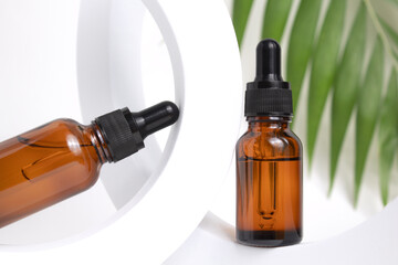 Amber glass dropper bottles different sizes on round form on white background with leaves. Cosmetic container mock-ups. Background for branding and packaging presentation. 