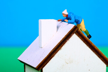 Conceptual image of a miniature figure man on the roof of a model house