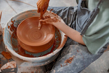 Young potter working on potter wheel in workroom
