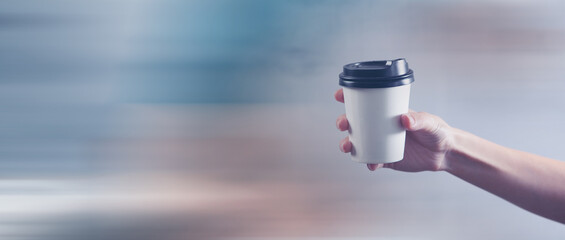 a female hand holds a disposable cup of coffee