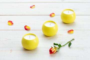 Naklejka na ściany i meble Three yellow scented candles on a wooden table. Rose petals are scattered on the table surface.