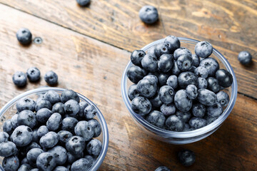 Fresh blueberries in a glass bowl and scattered on a wooden table. Foods containing antioxidants.