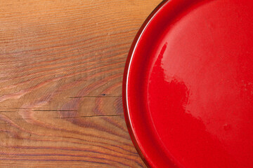 Fragment of a red empty ceramic plate on a wooden table. View from above.