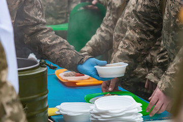 A field kitchen cook pours food for soldiers at a halt.