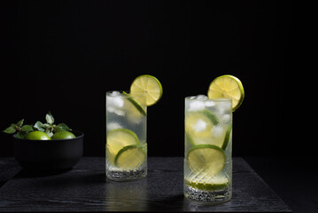 Dos vasos de refrescante cóctel de desintoxicación de jugo de lima con rodajas de lima y hielo sobre fondo negro	
