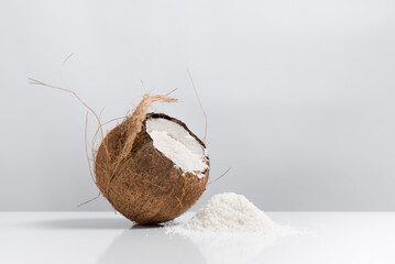 Coco abierto con hojuelas de coco ralladas que se derraman sobre una mesa blanca	