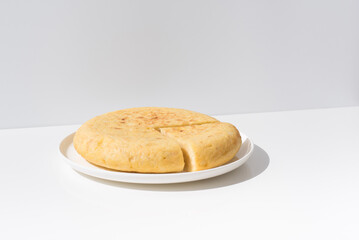 Tortilla de patatas española hecha con aceite de oliva, huevos y patatas en un plato blanco sobre una mesa blanca. Aperitivo español	