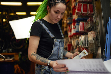 Tattooed woman checking information in book in garage