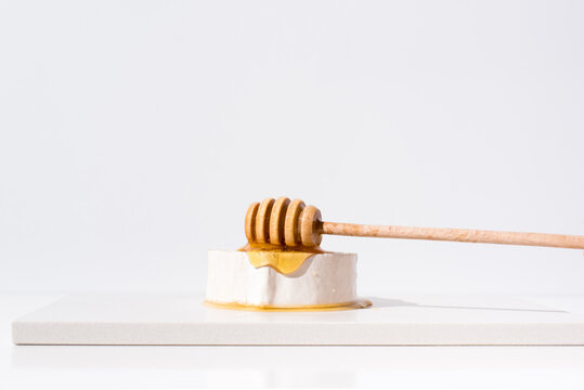 Verter la miel sobre el queso de cabra, con gotero de madera. Aperitivo comida mediterr&aacute;nea sobre fondo claro	