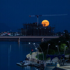 Full moon rising behind building under construction on a lake
