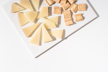 Trozos de queso manchego de oveja curado con tostadas de pan crujiente sobre una mesa blanca. Tapas españolas, Vista superior