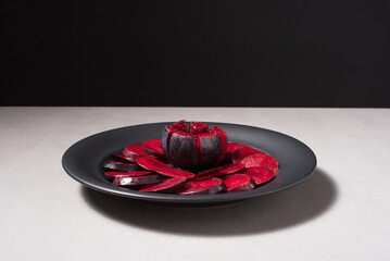 Rodajas de ciruelas negras y ciruelas enteras en un plato negro sobre una mesa gris	