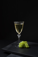 Una copa de vino blanco Verdejo español y un racimo de uvas de cosecha en una mesa de madera negra...