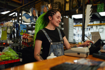 Positive young woman using cash register during work - obrazy, fototapety, plakaty