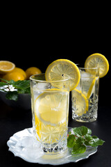 Dos vasos de refrescante zumo de limón, cóctel de frutas con rodajas de limón y hielo sobre fondo negro	
