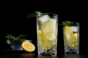 Dos vasos de refrescante zumo de limón, cóctel de frutas con rodajas de limón y hielo sobre fondo negro	