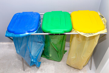 Three garbage bags for segregating glass, foil and paper standing on a rack in the garage with the lid closed.