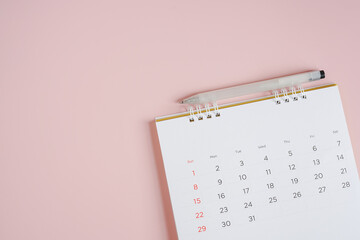 white opened monthly calendar and white pen on sweet pink background with copy space
