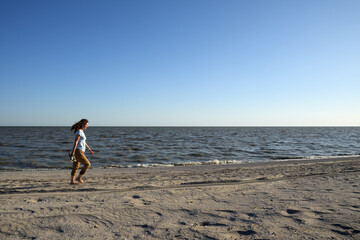 Woman walking along deserted sea beach in evening - 483577399