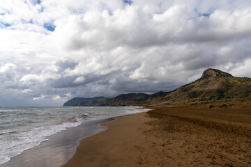 Fototapeta na wymiar golden brown sandy beach landscape with mountain landscape behind under an expressive sky