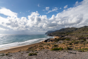 rocky ocean coast with mountains and a beautiful golden sand beach in the foreground